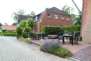 A brick house with a paved patio, outdoor seating, and a garden with lavender. - Schöne Og-ferienwohnung für 4 Personen an der Uttumer Mühle (Krummhörn)