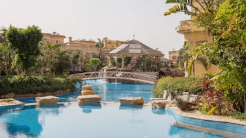 A swimming pool with rock formations, a bridge, and lush greenery.