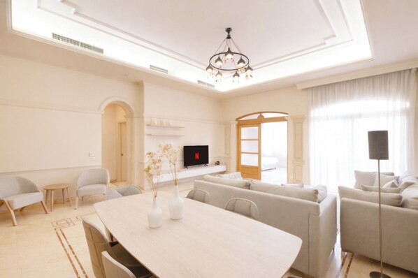Una sala de estar moderna con comedor, televisor de pantalla plana y candelabro.