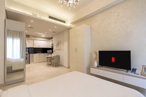 Una habitación de hotel con cama, un televisor mostrando el logotipo de Netflix, una zona de comedor con mesa y sillas, y una cocina al fondo.
