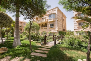 Un hotel de varios pisos con un jardín que incluye un puente de madera, escalones de piedra y abundante vegetación.