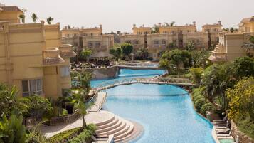 Un resort con una piscina central conectada por un puente, rodeado de exuberante vegetación y varios edificios con balcones.