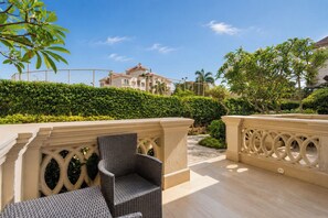 A patio area with a wicker chair, a stone balustrade, and a view of a large building in the background. - El Safwa Resort (New Cairo)