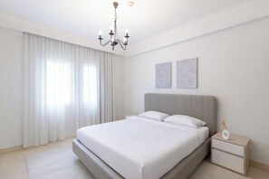 Un dormitorio moderno con una cama grande, una mesita de noche, una lámpara de pared y dos cuadros decorativos.