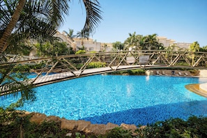 Una piscina con un ponte, circondata da palme e un edificio sullo sfondo.