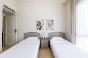 Habitación de hotel con dos camas, una mesita de noche con un jarrón y arte abstracto en la pared.