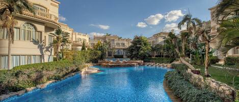 A resort with a central swimming pool, palm trees, and Mediterranean-style buildings.