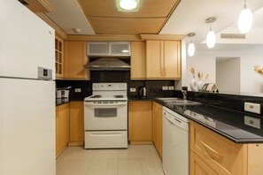 Cocina compacta con estufa, horno y lavavajillas, muebles de madera y encimera negra.