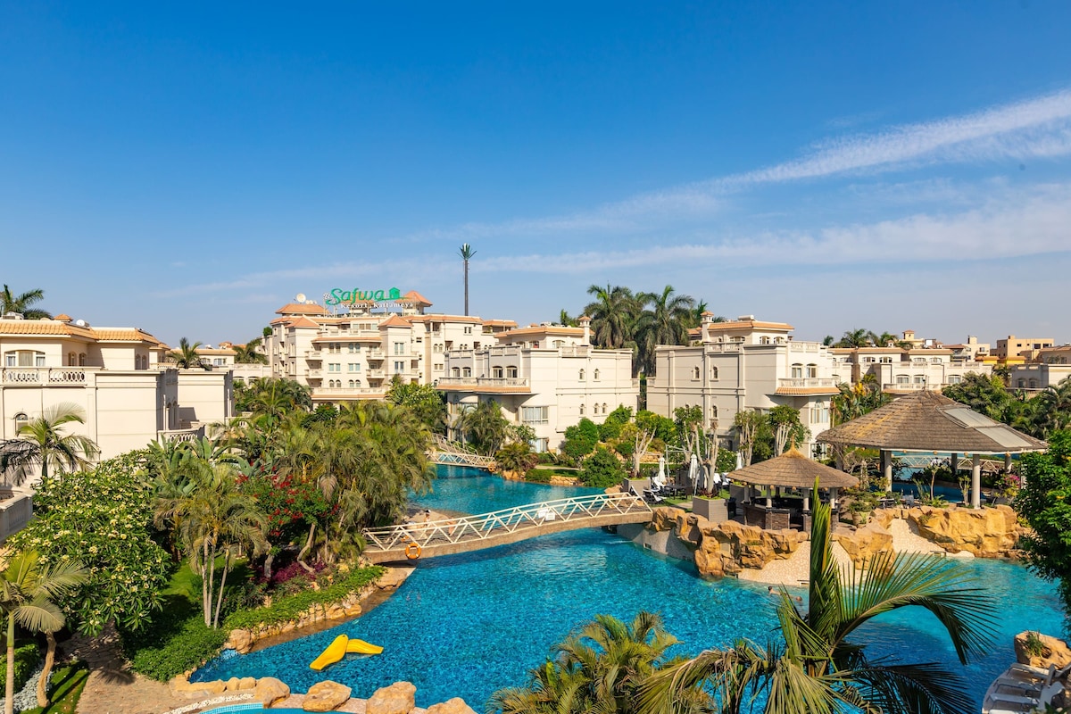 A resort with a swimming pool, palm trees, and a bridge.