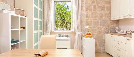 A cozy kitchen with a stone wall, a window with curtains, a white cabinet, and a fruit bowl on the counter.