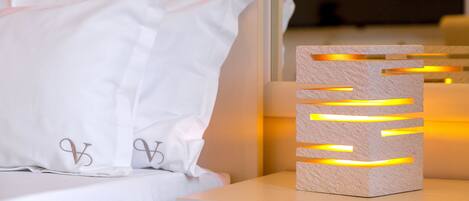 A neatly made bed with white linens and pillows, a bedside table with a modern light fixture, and a wooden headboard.