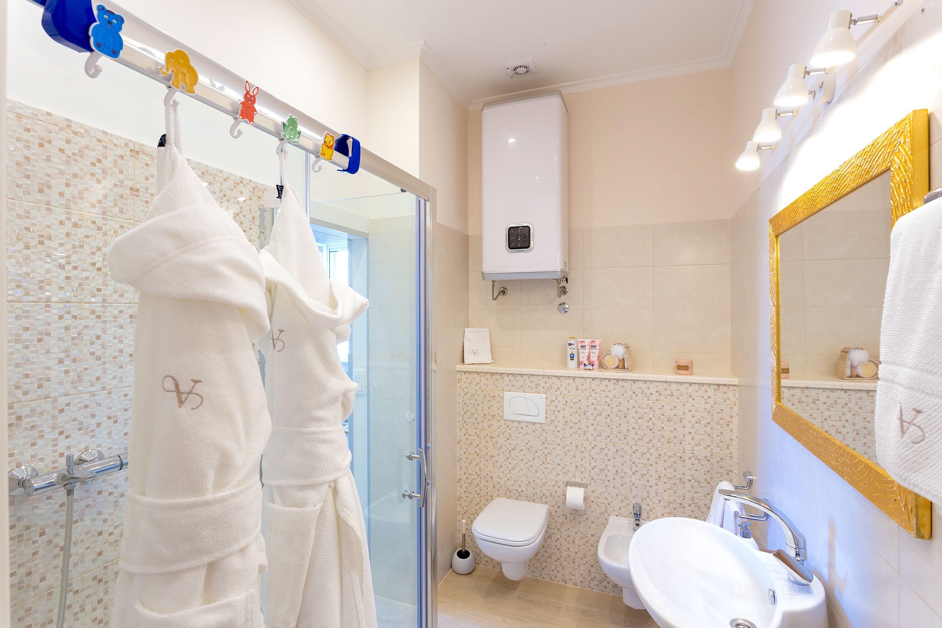 A bathroom with a glass shower enclosure, a toilet, a sink, and a mirror with a gold frame.