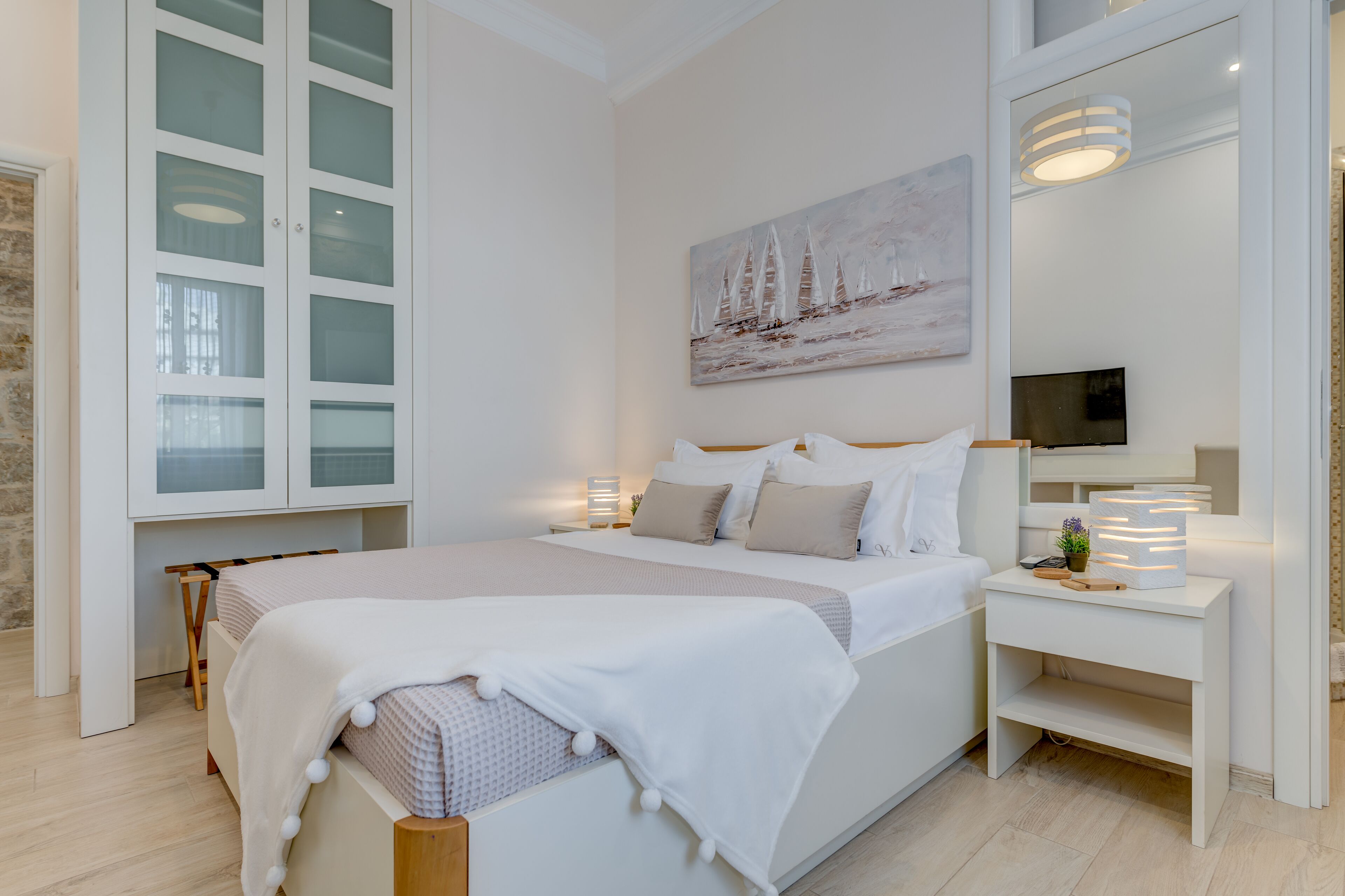 A modern bedroom with a large bed, a bedside table with a lamp, a TV, and a painting on the wall.