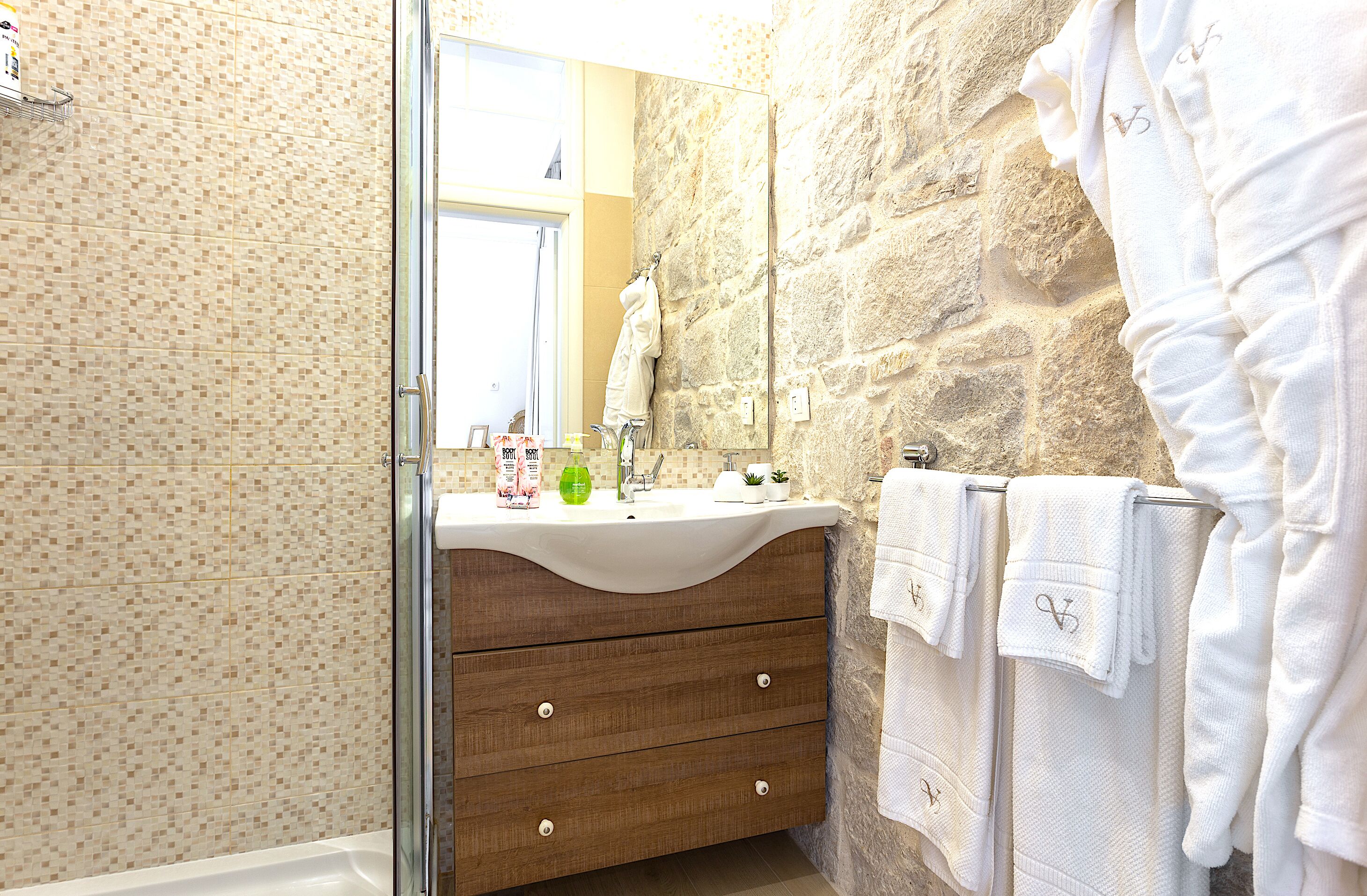 A bathroom with a stone wall, a wooden vanity, a glass shower enclosure, and multiple white towels.