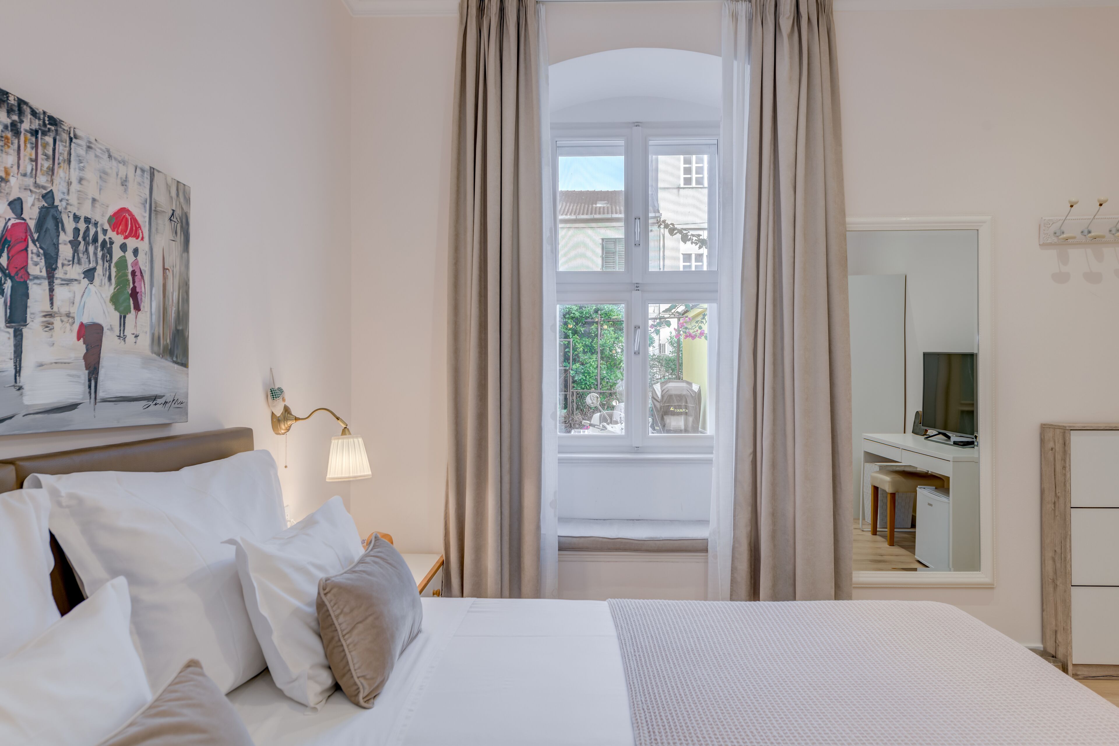 Habitación de hotel con una cama grande, un escritorio con silla, una lámpara de escritorio, un cuadro en la pared y una ventana con cortinas.