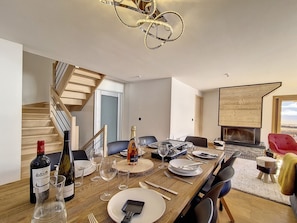 Uma sala de jantar com uma mesa de madeira posta para refeição, um candelabro e uma lareira.