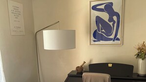 Ett hotellrum med en säng, ett skrivbord, en lampa, ett inramat konstverk, ett litet bord med ett ljus och en skylt som är upphängd på väggen.