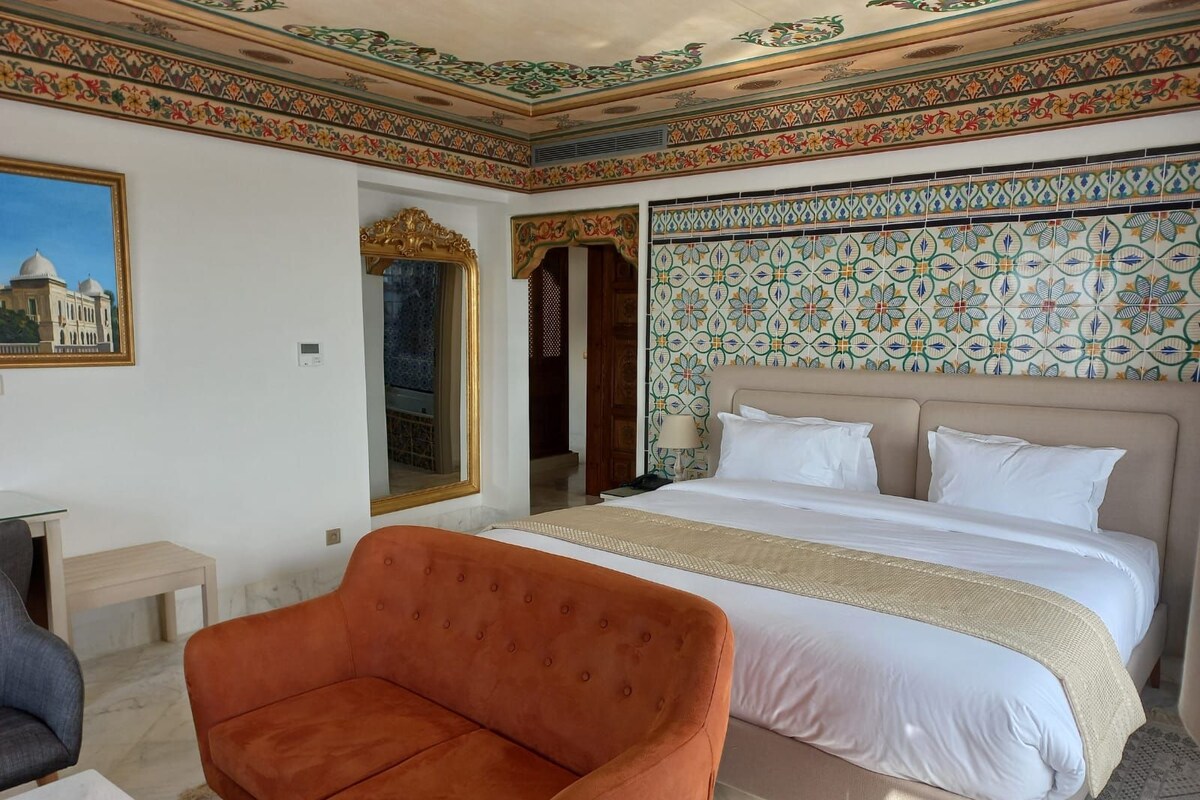 Habitación de hotel con una cama grande, un sofá, un escritorio y un papel tapiz estampado.