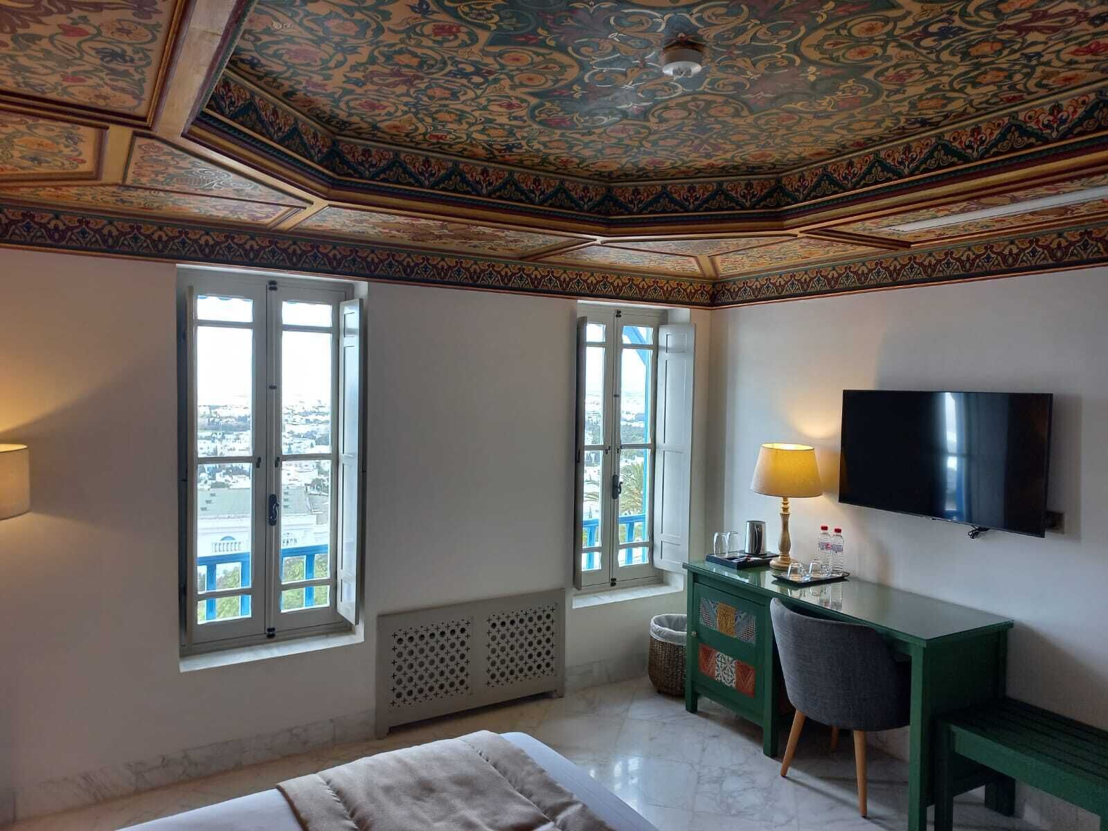 Een kamer met een bed, een bureau, een stoel, een televisie en twee ramen met uitzicht.