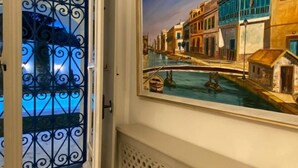 Un pasillo con una puerta adornada con una celosía metálica, un cuadro que muestra una escena de canal y un piso de mármol.