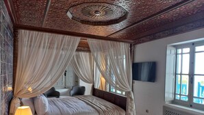 Una cama con dosel, cortinas translúcidas, una lámpara de noche y un televisor montado en la pared.