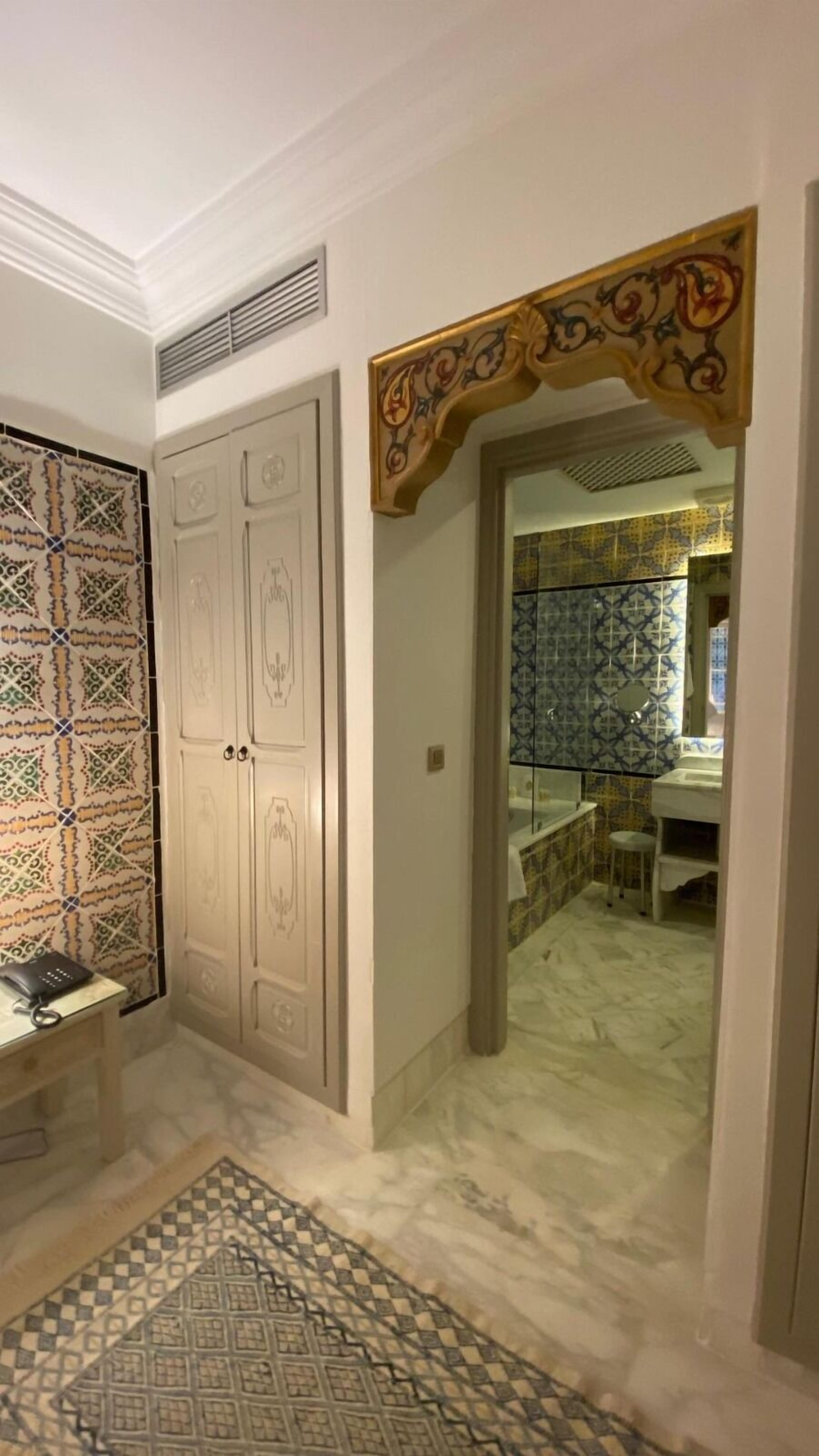Un corridoio con piastrelle decorate, pavimento in marmo e un arco decorativo che conduce a un bagno con piastrelle decorate e un lavandino.