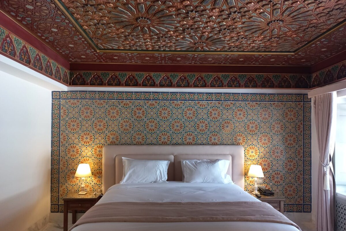 Una habitación de hotel con una cama grande, dos lámparas de noche y un techo decorativo.