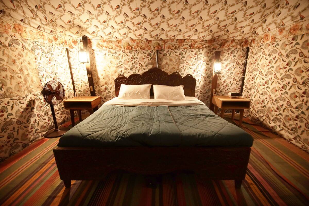 A room with a bed, two bedside tables, a floor lamp, and patterned wallpaper.