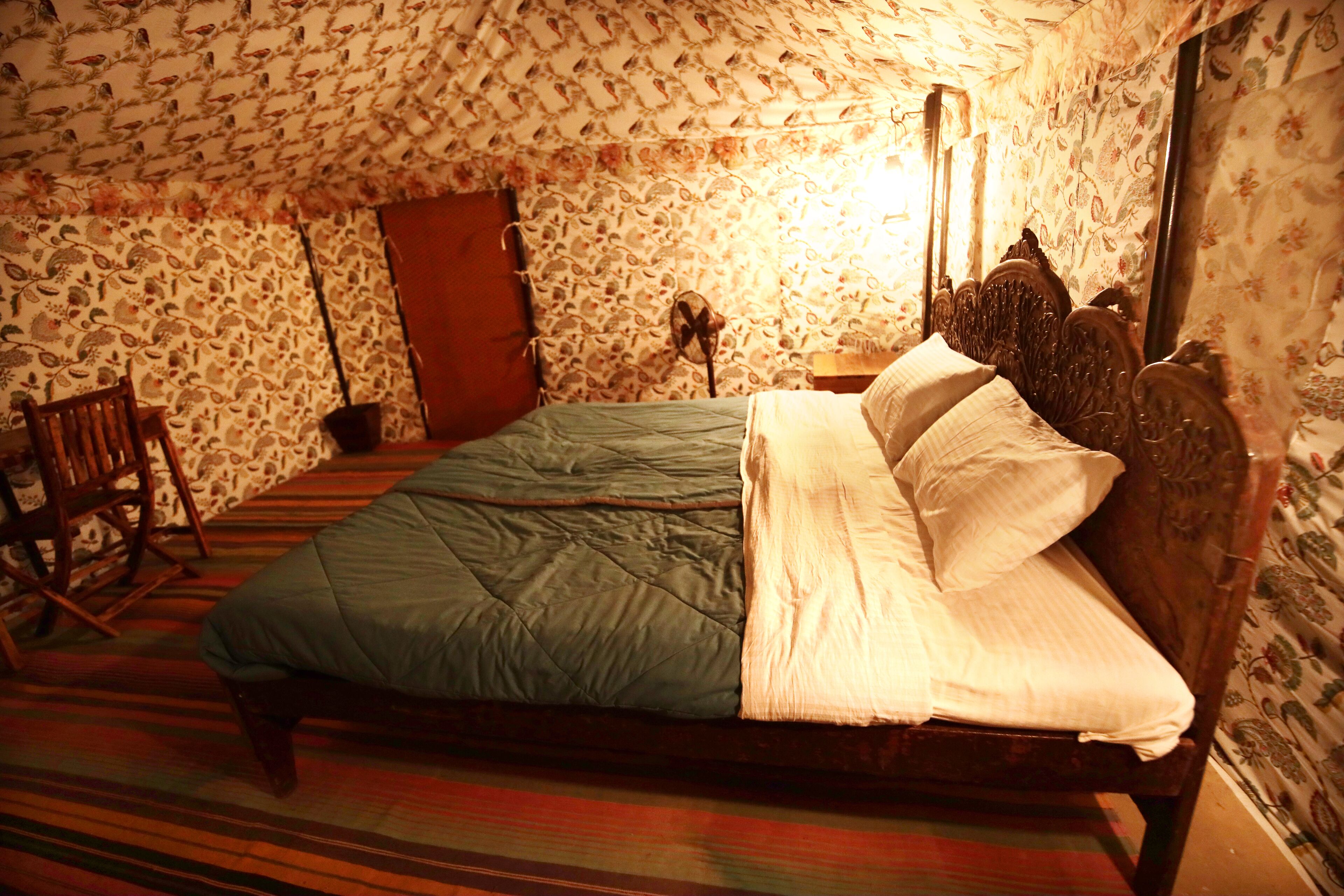 A room with a bed, a chair, and patterned wallpaper.