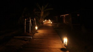 A wooden pathway leading to a building at night, illuminated by lanterns.