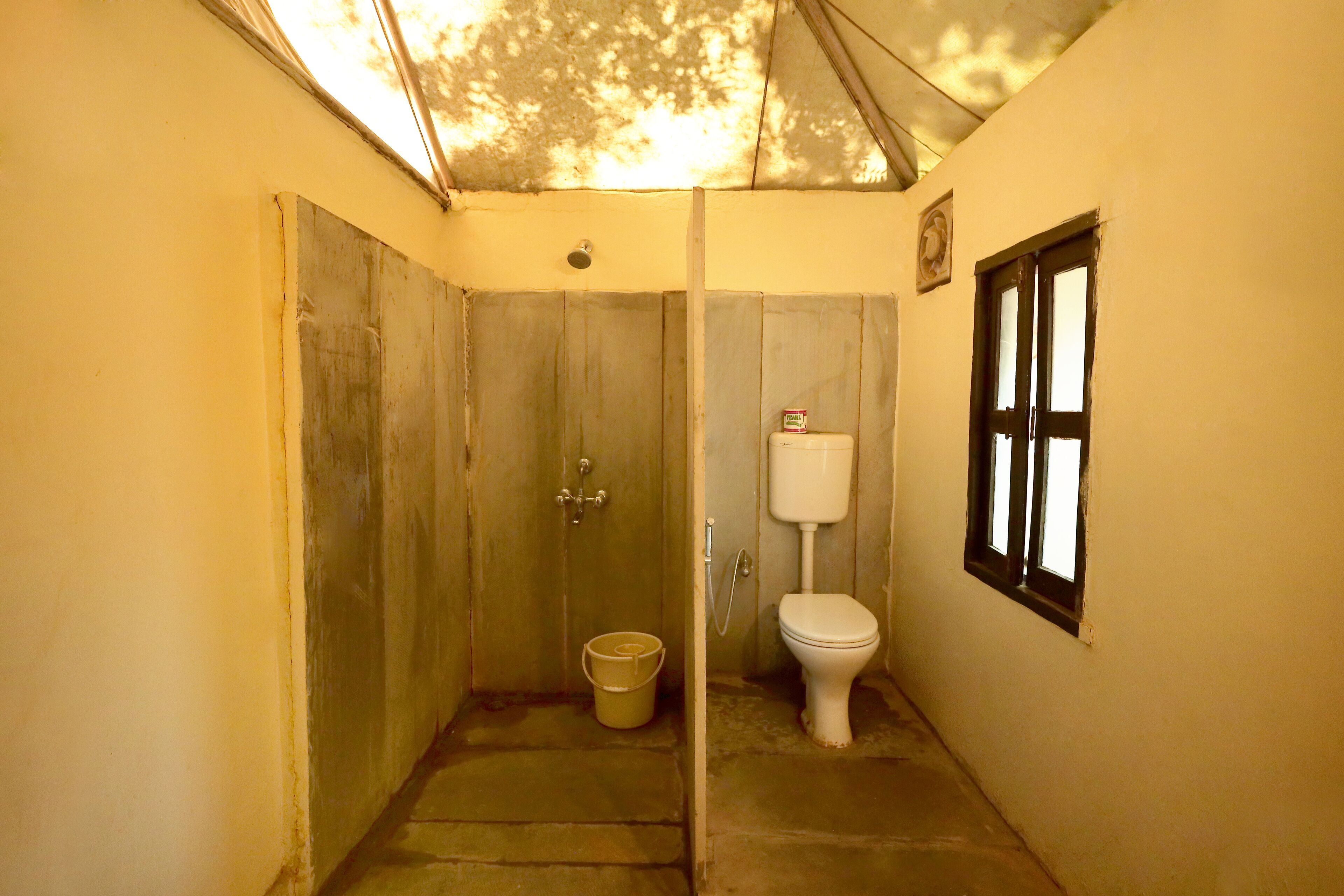 A small, narrow bathroom with a toilet and a bucket on the floor.