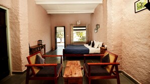 A bedroom with a bed, two wooden chairs, a wooden table, and a window with curtains.