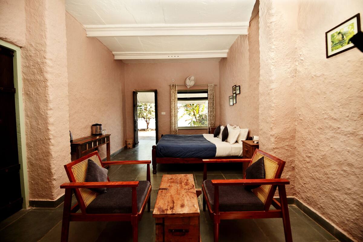 A bedroom with a bed, two wooden chairs, a wooden table, and a window with curtains.