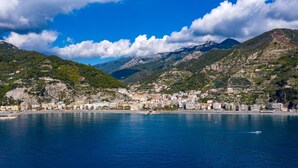 A coastal town with buildings along the waterfront, a clear blue sea, and mountains in the background.