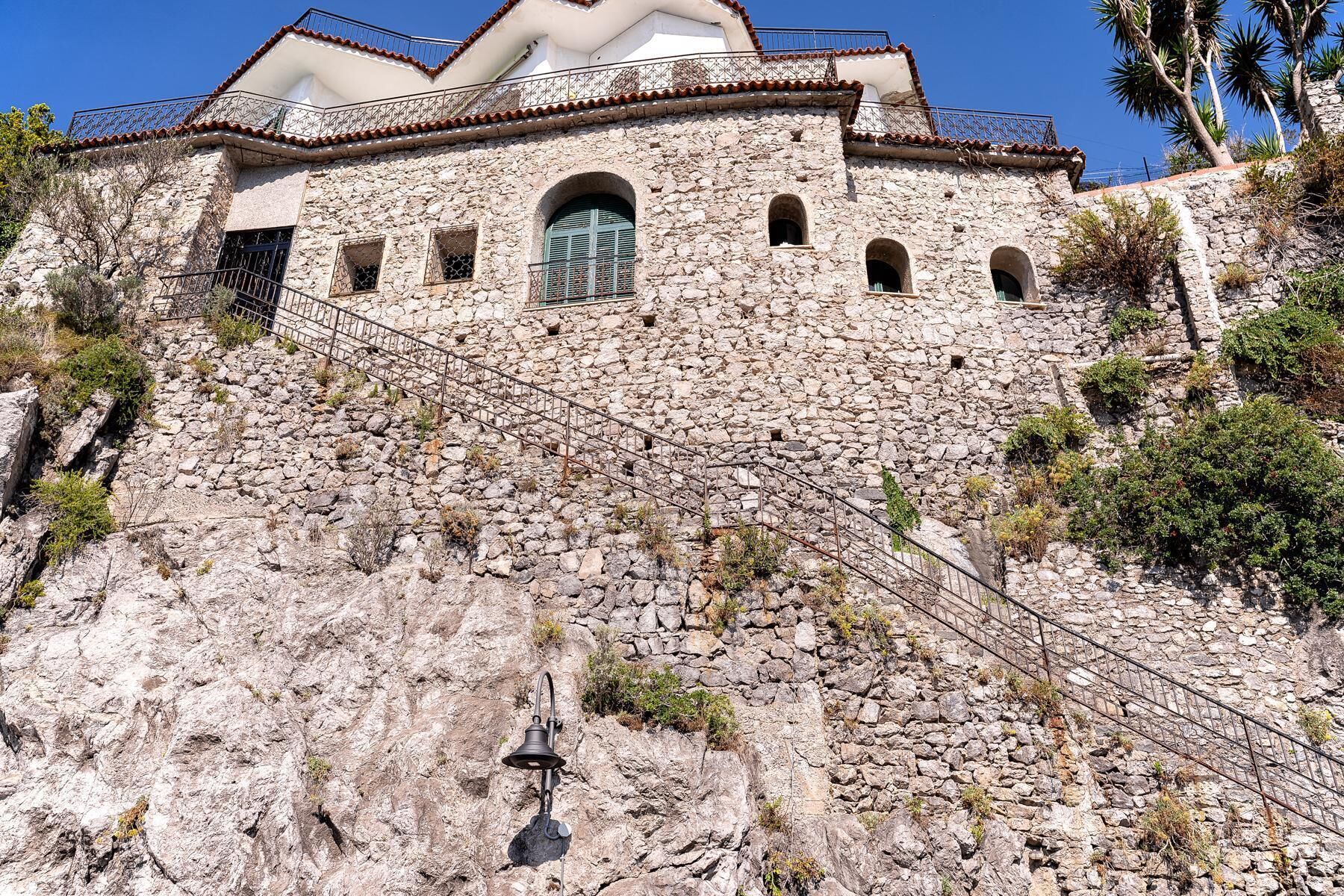 A stone building with a bell tower, arched windows, and a staircase leading up to a door.