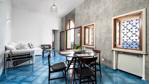 A modern living room with a blue-tiled floor, a white sofa, a black chair, and a dining table with chairs.