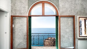 A room with a large arched doorway leading to a balcony with a view of the sea.