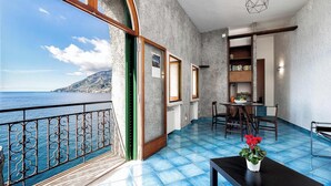 A balcony with a view of the sea, a dining area with chairs and a table, and a bookshelf.