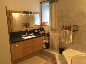 Un baño con tocador de madera, lavamanos, espejo, toallero y retrete.