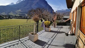 A balcony with a view of a mountain range, a grassy field, and a building with wooden doors. - Beautiful building at the foot of the mountains, 15kms from Lake Annecy,  (Ugine)