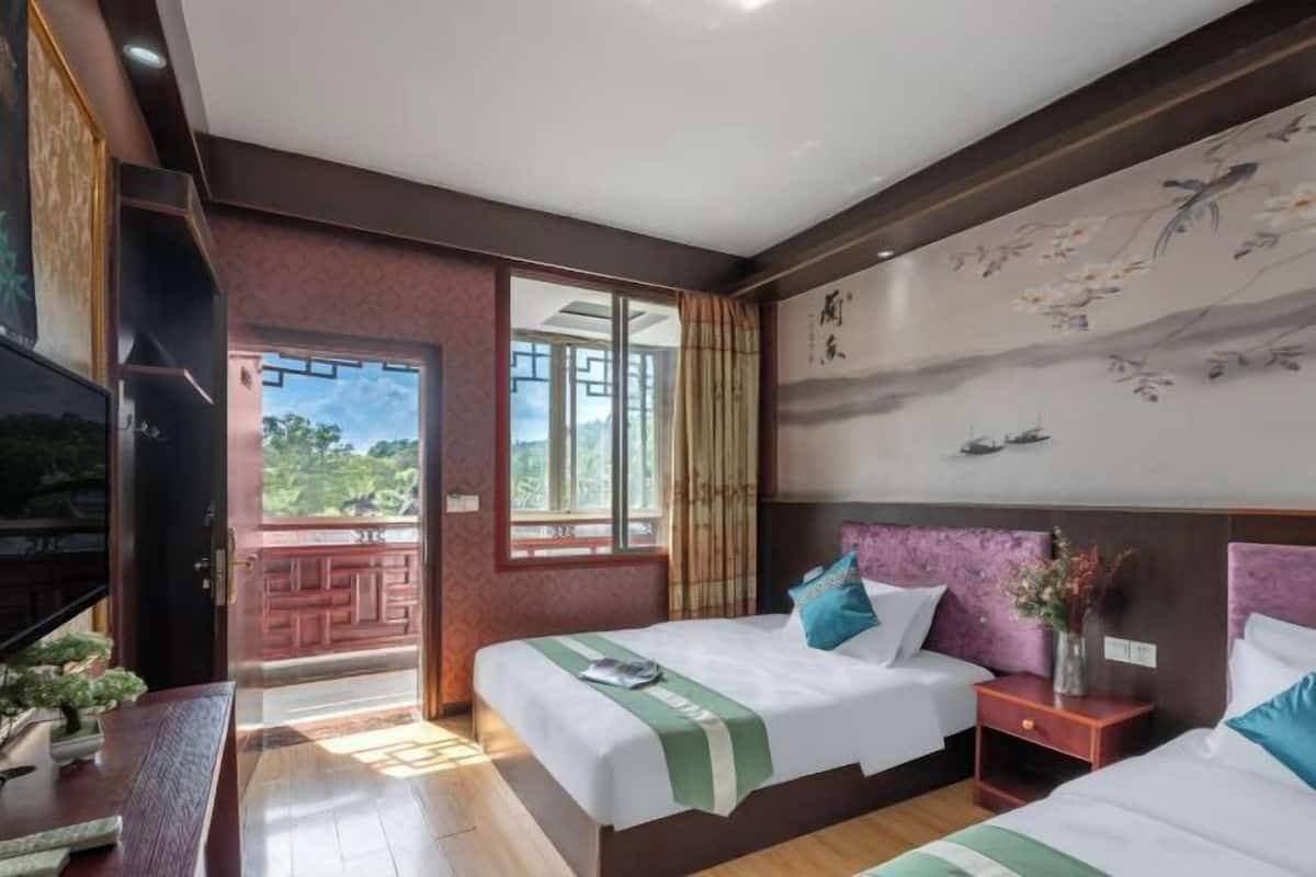 Une chambre d’hôtel avec deux lits, une grande fenêtre, un tableau au mur et un téléviseur placé sur le côté gauche.