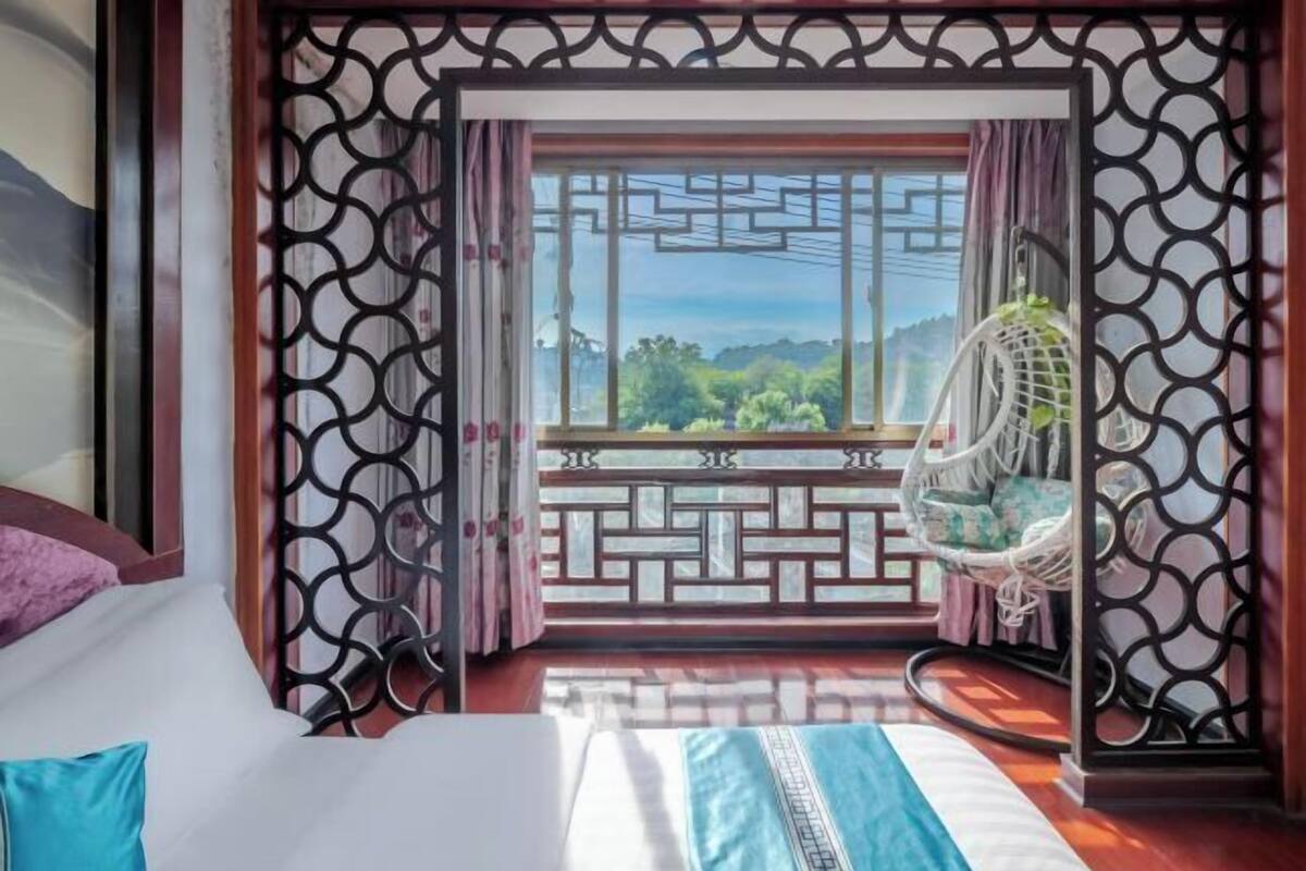 Une chambre avec un lit, une vue sur la verdure par la fenêtre et un fauteuil suspendu.