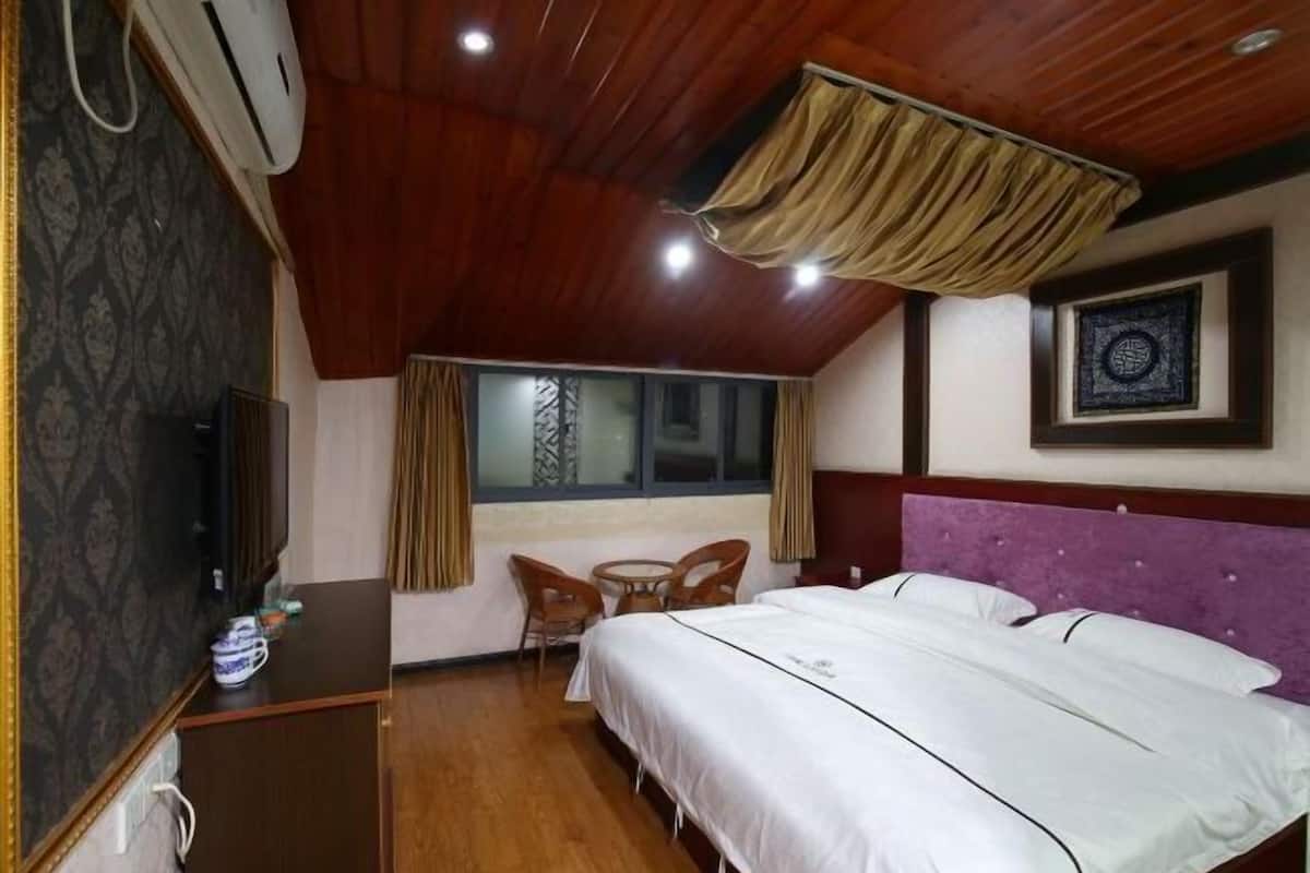 Une chambre d’hôtel avec un plafond en bois, un lit avec une literie blanche, une petite table avec des chaises et une fenêtre avec des rideaux.