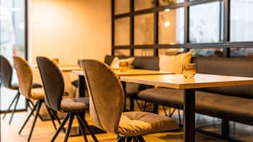 Un comedor moderno con una mesa de madera y sillas acolchadas, un sofá y un ventanal con persianas.