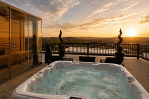 A hot tub on a balcony with a view of the sunset and distant landscape.
