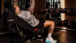 A person performing a bench press exercise in a gym with various dumbbells and weight plates. - Luma Hotel Spa&Fitness (Fulda)