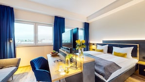 A hotel room with a bed, bedside table, TV, and a view of the city. - Luma Hotel Spa&Fitness (Fulda)