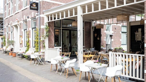 A brick building with a covered outdoor seating area featuring white tables and chairs.