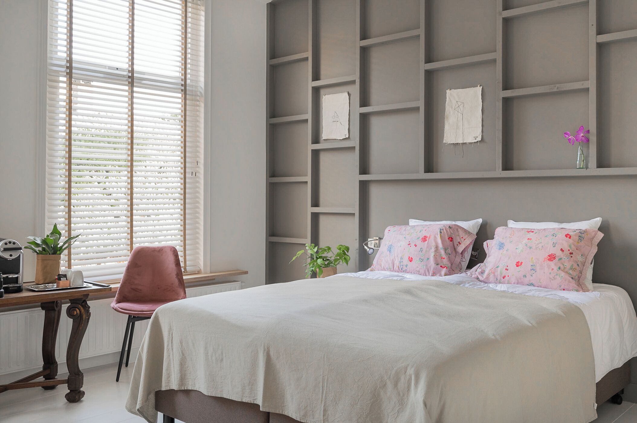Een slaapkamer met een bed, een bureau met een plant en een raam met jaloezieën.