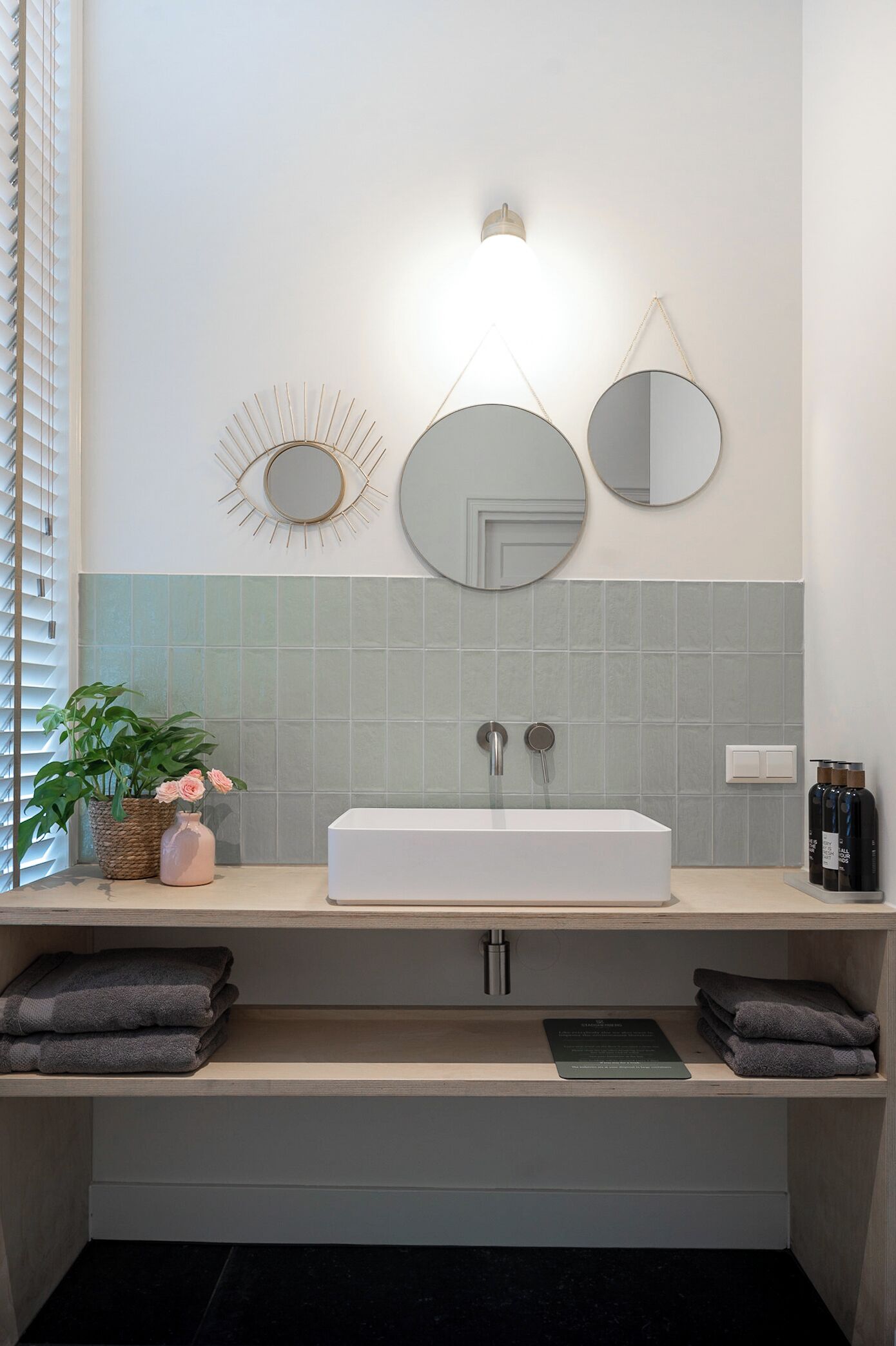A bathroom with a white sink, two mirrors, a wall-mounted light, and a potted plant.